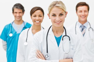 Beautiful young doctor standing with hands folded and assistant doctors in background